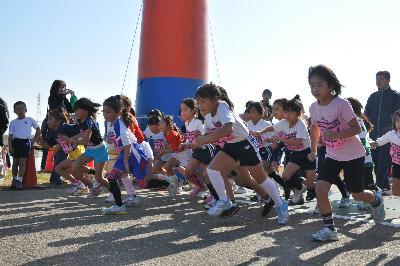 大人たちが見守る中で大勢の子供たちが左のほうに向かって走り出している姿を捉えた写真