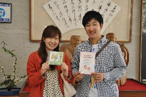 立派な額が飾られた雅やかな部屋の前で、謡曲「高砂」のCDを持って微笑んでいる夫婦の写真