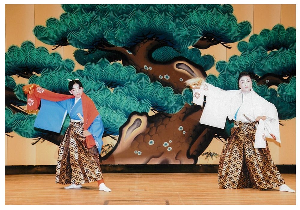 3人の演者が、松が描かれている扇子を広げ、両手に持ちながら踊っている様子