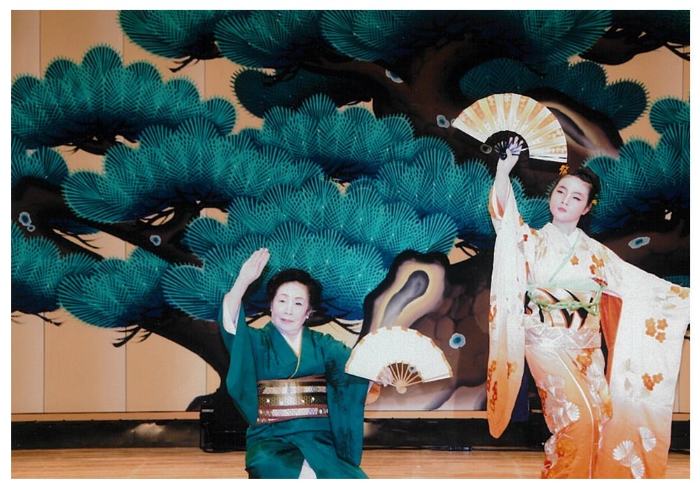 橙色の衣装を着た3人の演者が両手を横に広げ、上下に動かして踊っている写真