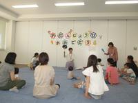 壁に、お誕生日おめでとう、と書かれた部屋で、小さな子を中心にして複数の親子が円になって座っている写真