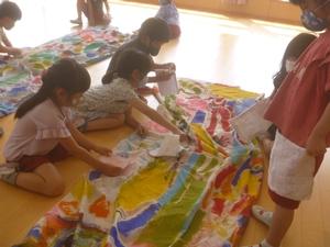 室内の床に広げられたこいのぼりをとり囲み、手にした雑巾でそれを拭いている子供たちの写真