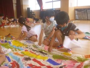 床に広げられたこいのぼりの側に座り込み、雑巾でそれを拭いている子供たちの写真