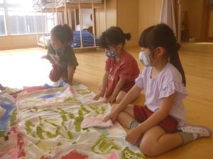 床に広げられたこいのぼりの側に座り込み、雑巾でそれを拭いている3人の女の子たちの写真