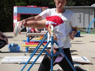 高砂児童学園の園庭で男性の先生に手伝ってもらいながら鉄棒をする女児の写真