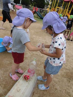 作った色水をろうとをつかってペットボトルに入れている子供の写真
