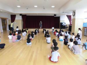 一定の距離を保ちながら体育すわりで並び、先生の話を聞いている子供たちの写真