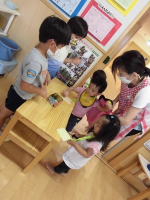お店屋さんごっこをする年長の子供の元に、お客さん役の年少の子供がやってくる写真