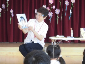 体育館ホールで絵本の読み聞かせをする教師の写真