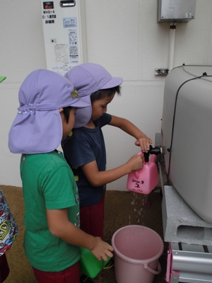 雨水貯留タンクからジョウロに水をくむ子供たちの写真
