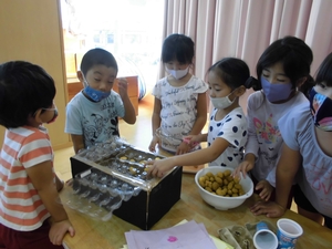 空き箱と卵パックを使ってカステラを焼いて売るごっこ遊びをする子供たちの写真