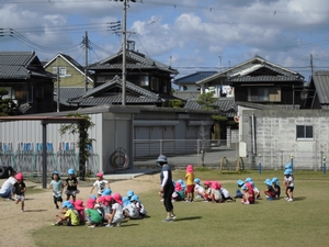 青空の下かけっこをする子供たちと、座って順番待ちをする子供たちの写真