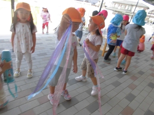 女の子が手にかかげた紫、青、ピンクのビニールテープが、リボンの様に風にたなびいている写真