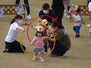 お面をつけてリングをくぐる幼児たちの写真