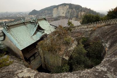 宝殿山中腹地点より俯瞰で撮影された、生石神社本殿の背面と石の宝殿の写真。写真の奥には竜山の遠景も確認できる