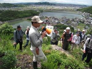 高御位山の、ため池を一望する場所で先生の話を聞く参加者たちの写真