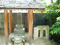 小さな東屋の屋根の下で花を供えられた顕彰墓の写真