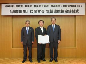 高砂市長と高砂商工会議所会頭が両脇に立ち、中央で但陽信用金庫理事長が協定書をこちらに見せている写真