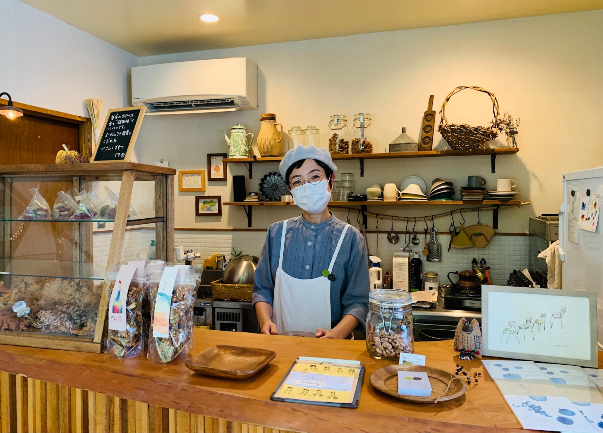 お菓子が陳列された温かみを感じる木製のカウンターで微笑むエプロン姿の女性