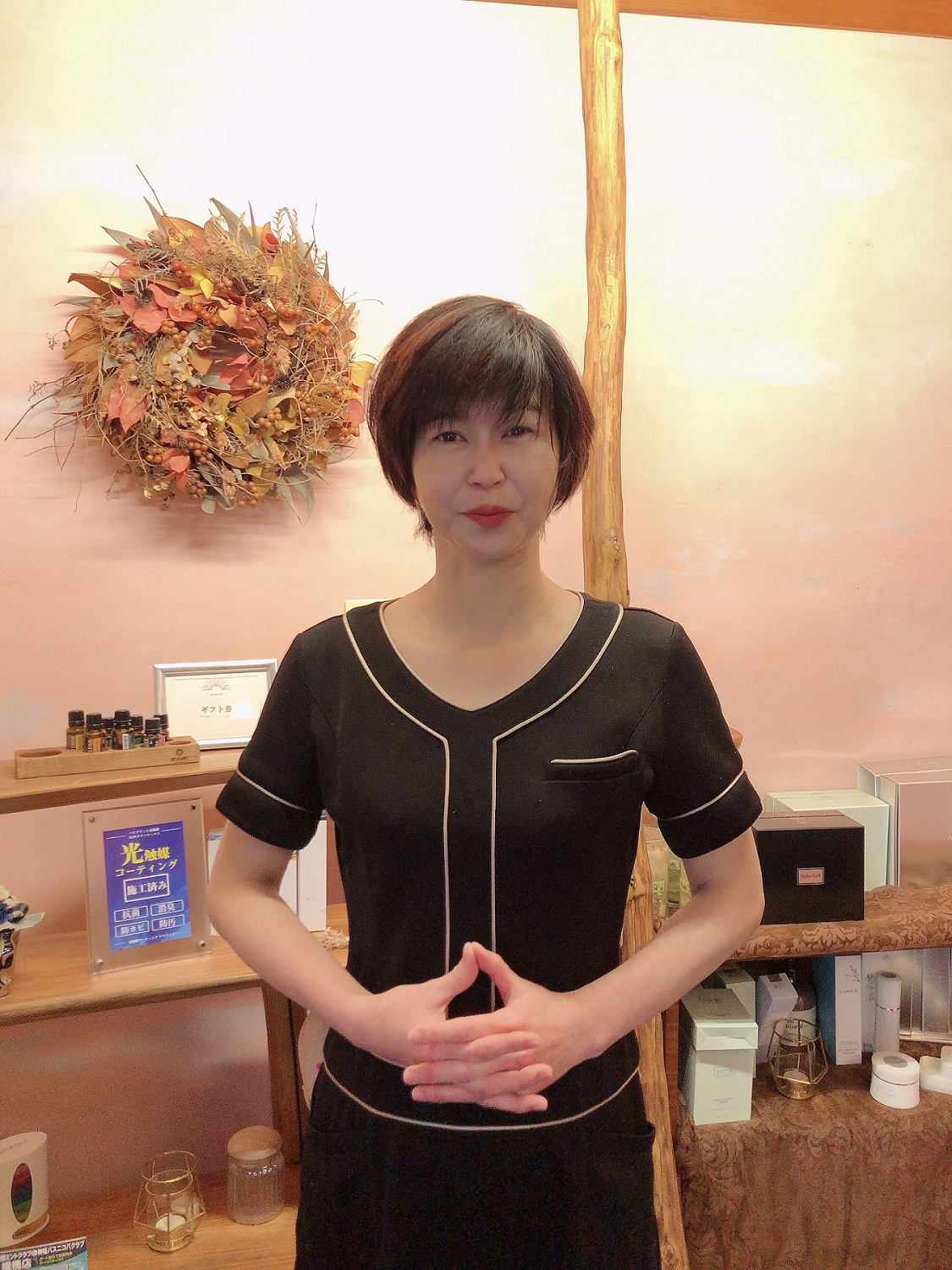 温かみを感じるエステサロンの店舗内で両手を前にして立つ黒い服の女性