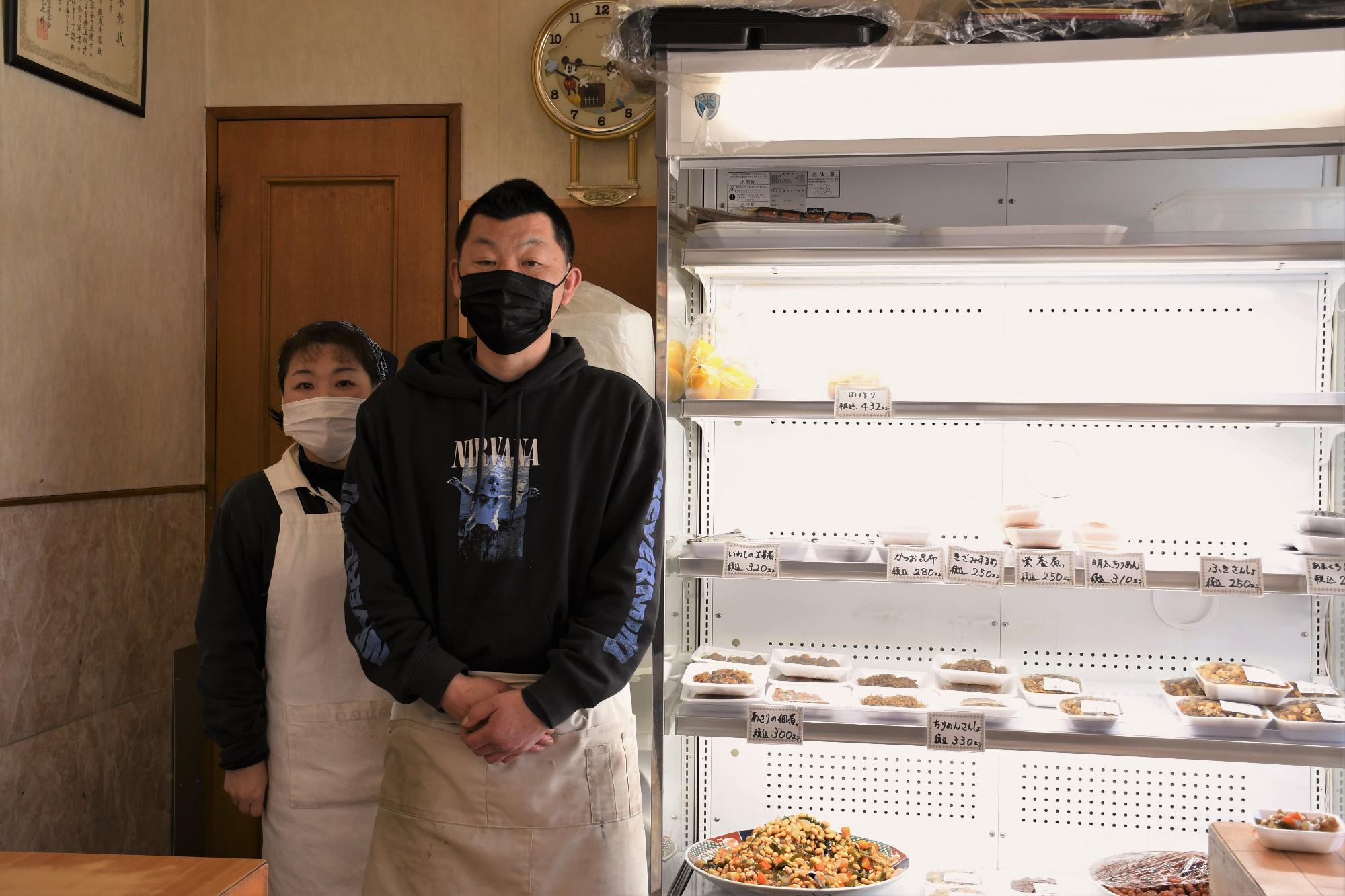 惣菜が並ぶ陳列棚の前に立つ男女の写真