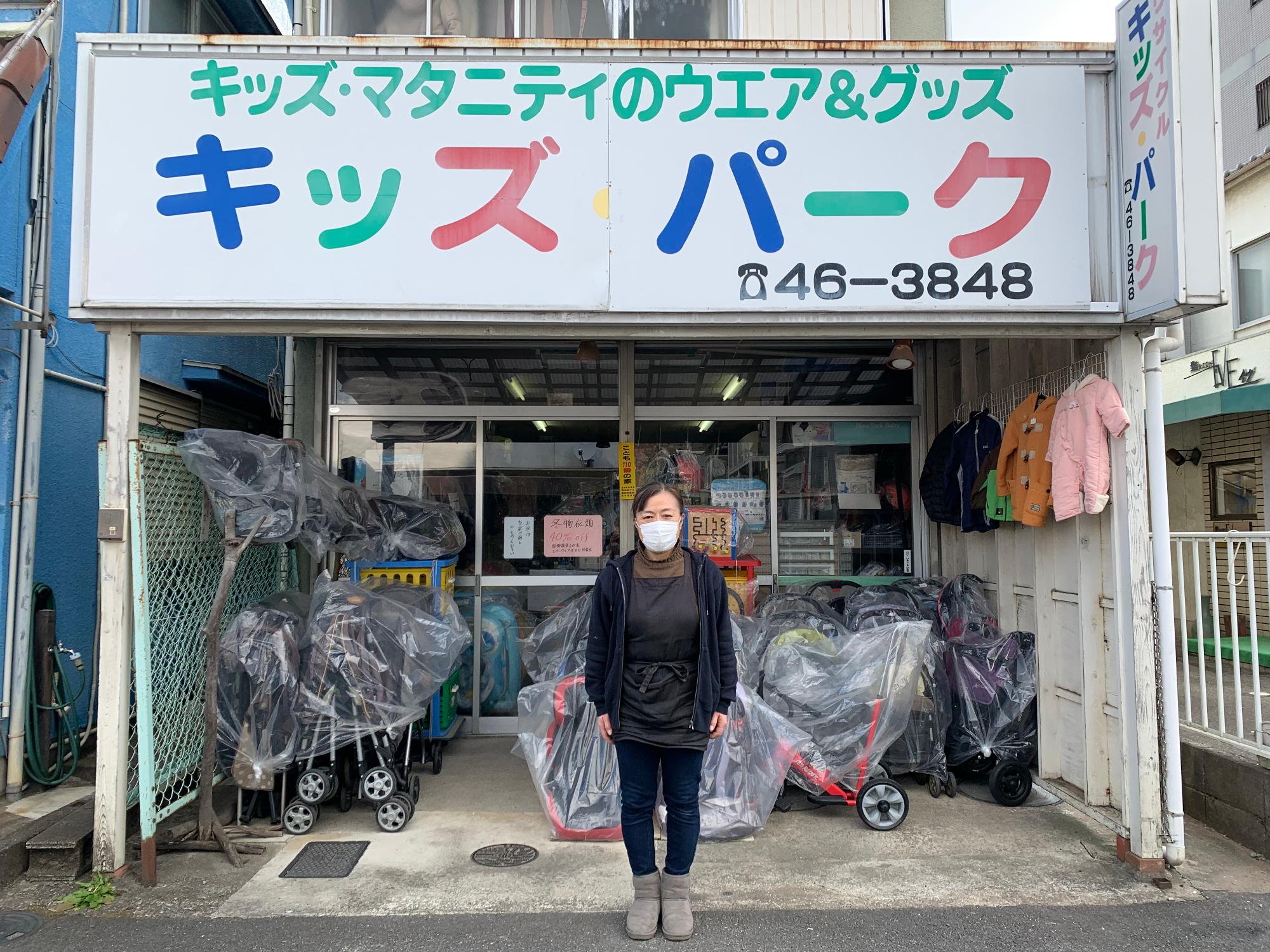 子ども用品、マタニティ用品を取り扱うリサイクルショップの大きな看板の前に立つ女性