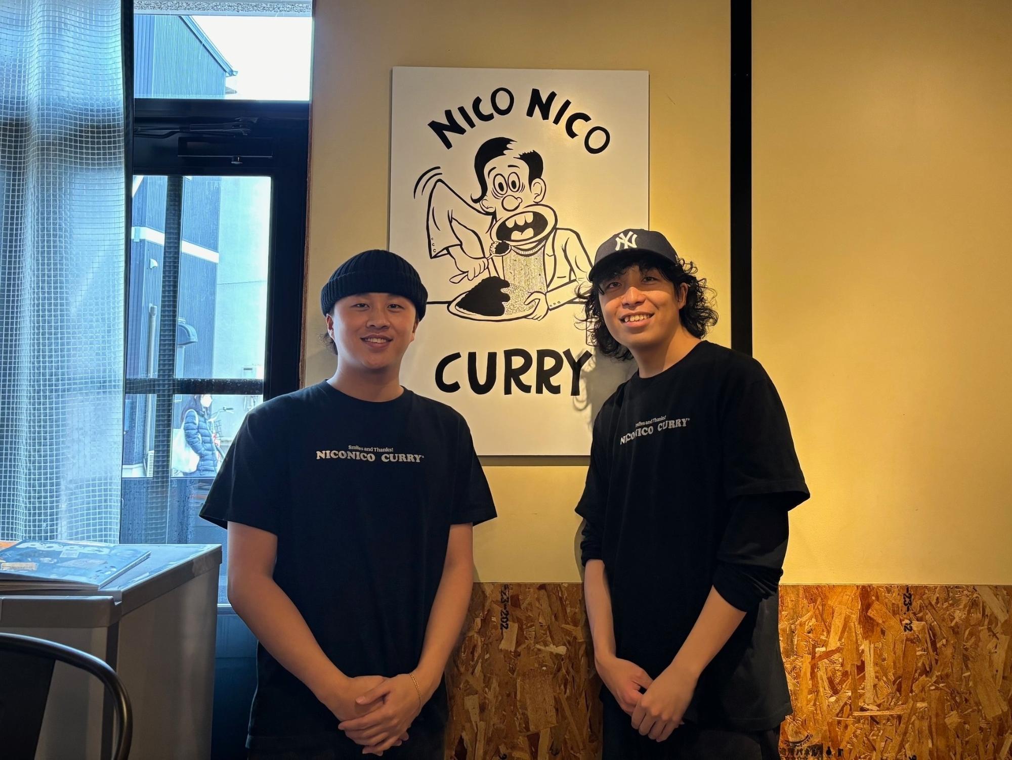 ニコニコカレーの店内で笑顔で並ぶ男性2人
