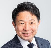 黒いスーツ姿で正面を向いている笑顔の芝本やすあき議員の写真