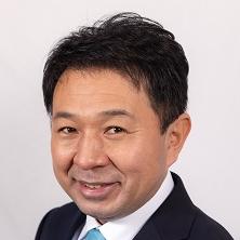 黒いスーツ姿で正面を向いている笑顔の芝本やすあき議員の写真