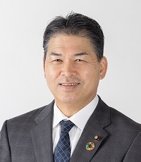 白い背景に黒いスーツ姿で正面を向いている真剣な顔の鷹尾治久議員の写真