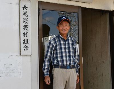 長尾楽笑村の看板が掲げられた建物の前で立つ男性の写真