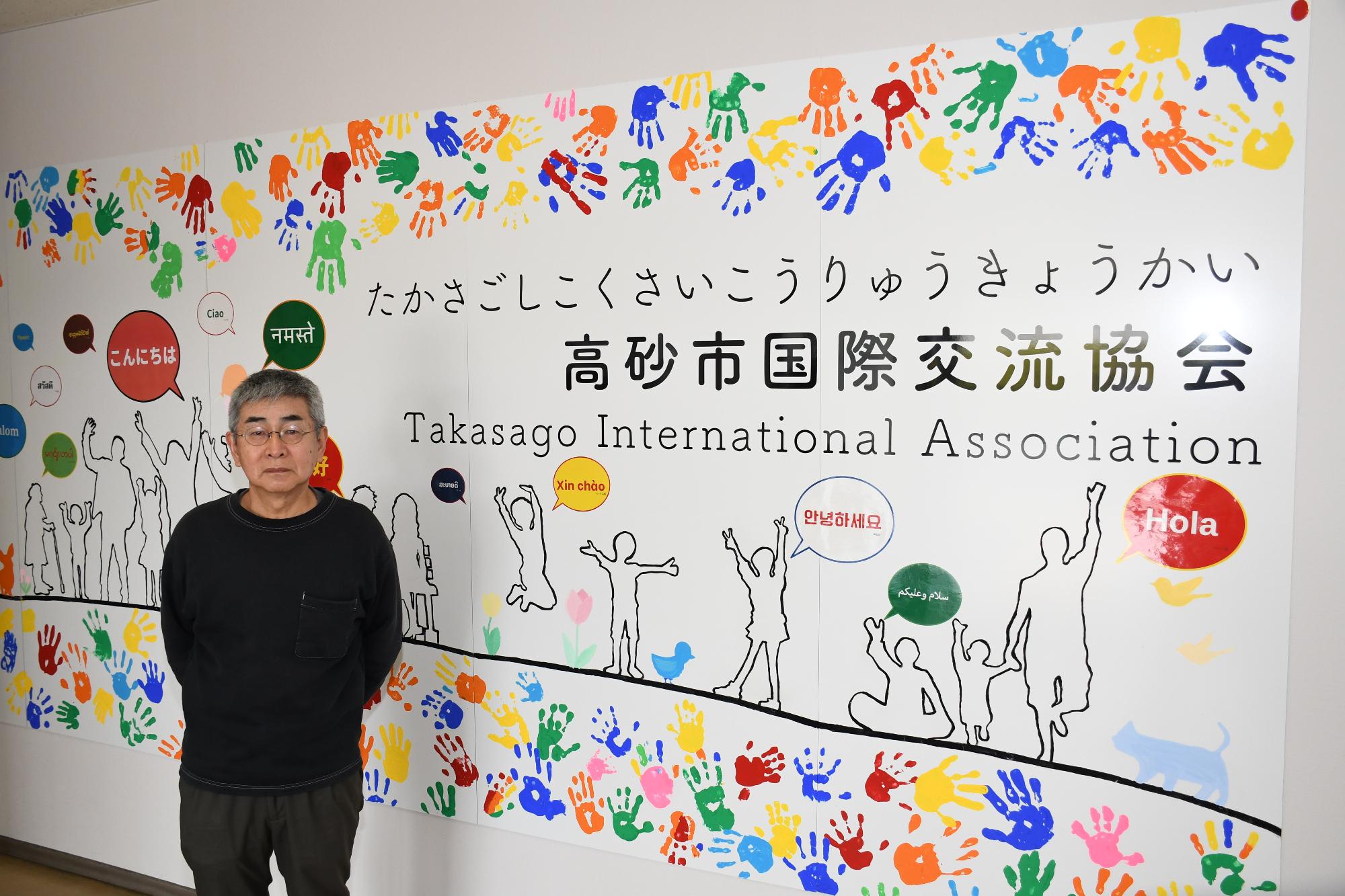 高砂市国際交流協会と書かれたカラフルな看板の前に立つ男性の写真