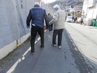 高齢の男性と、その男性の腕に手を添えて歩いている人の写真