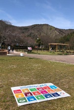 晴れた日に公園の芝生の上にひろげられたSDGsフラッグの写真