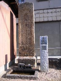 プレートが埋め込まれた石柱の隣に屋根と同じ高さの石碑が設置されている写真