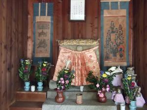 両側に掛け軸が飾ってあり花がお供えされているお堂内のお地蔵様の写真