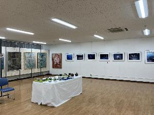 去年大賞を受賞した作品の展示場の様子。手前の机の上に彫塑工芸の作品が並んでおり、その後方で日本画と写真が展示されています。