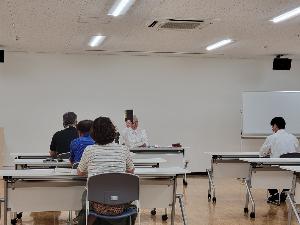 講師が資料を持ち上げて受講者に見せている様子