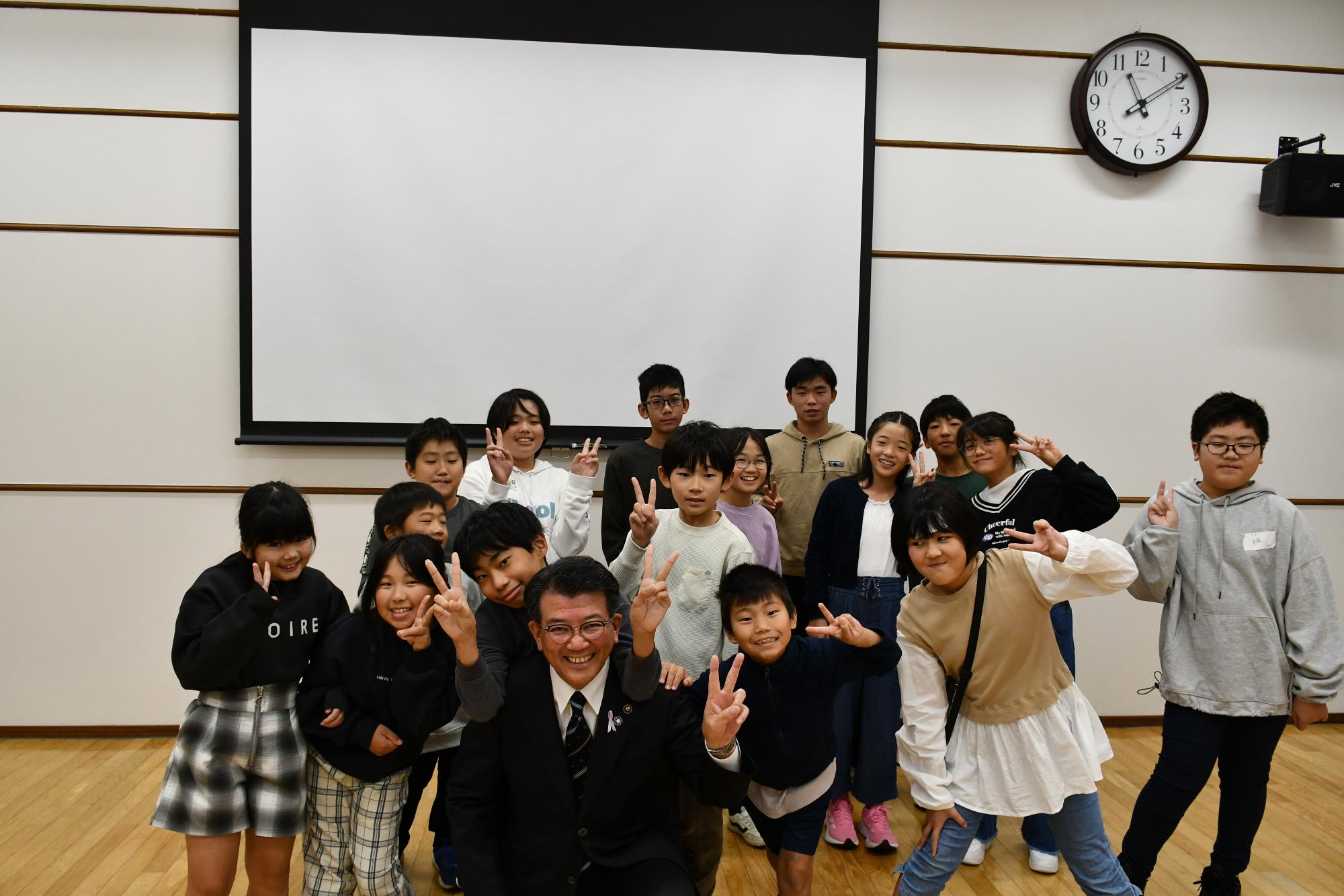 市長を中心にワークショップに参加した笑顔のこどもたちがペースサインで集合している写真