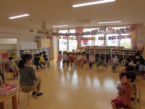 教室内で四角く椅子を並べて座り先生の話を聞く子供たちの写真