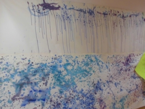 白い紙に子供たちが描いた、雨の様子を模して青や水色に彩られた絵の写真