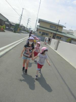 晴空の下、縦2列になり隣の子と手をつないで歩道を歩いてくる子供たちの写真
