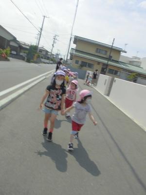 晴空の下、縦2列になり隣の子と手をつないで歩道を歩いてくる子供たちの写真