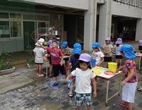 園庭で机の上に置かれたシャボン玉液に大きな輪を浸して思い思いにシャボン玉遊びを楽しむ園児たちの写真