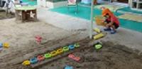 園の砂場でしゃがみながらカラフルな電車のおもちゃを繋げて貨物列車を作る男児の写真