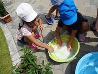 しゃがみながらシャボン玉の液を入れたボウルに右手で大きなシャボン玉用の輪を浸す女児と輪を両手で上から抑える男児の写真