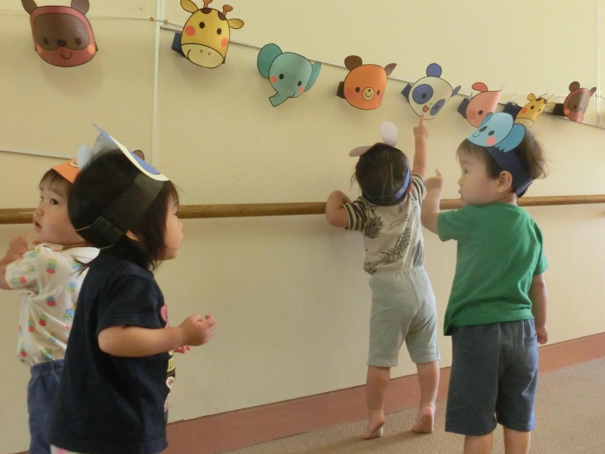 縁日ごっこで廊下に横1列に飾られた動物のお面に興味津々な頭に動物のお面を付けた園児4人の写真
