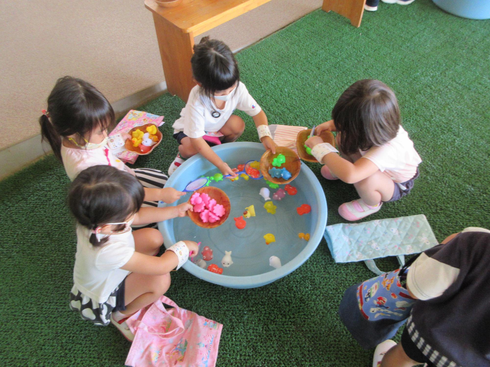 たらいに浮いているカラフルな金魚のおもちゃをポイですくってボウルに入れる女児4人を上から撮影した写真