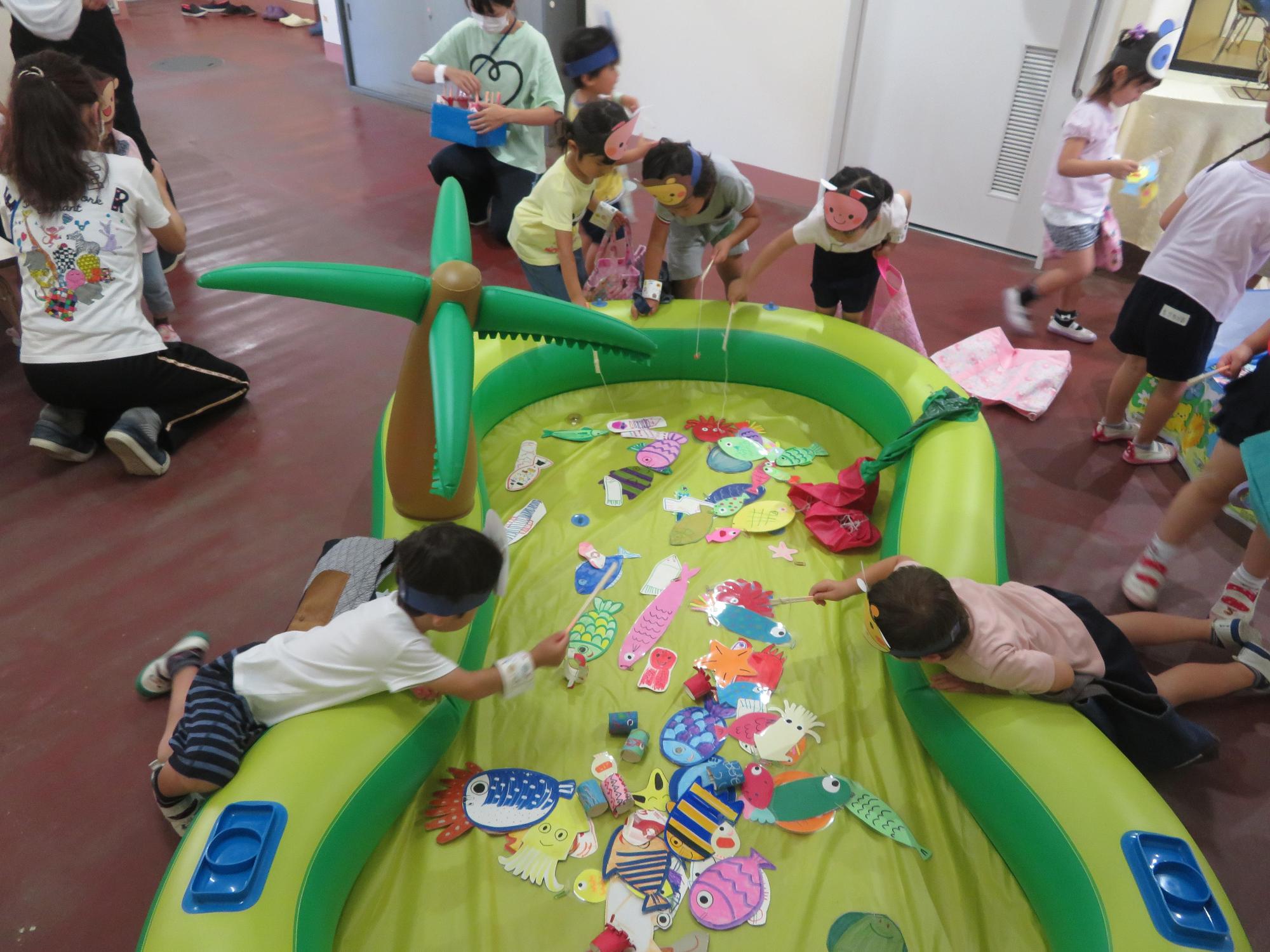 ビニールプールに入っている魚の絵を釣り竿で前屈みになりながら必死に釣る園児たちの写真