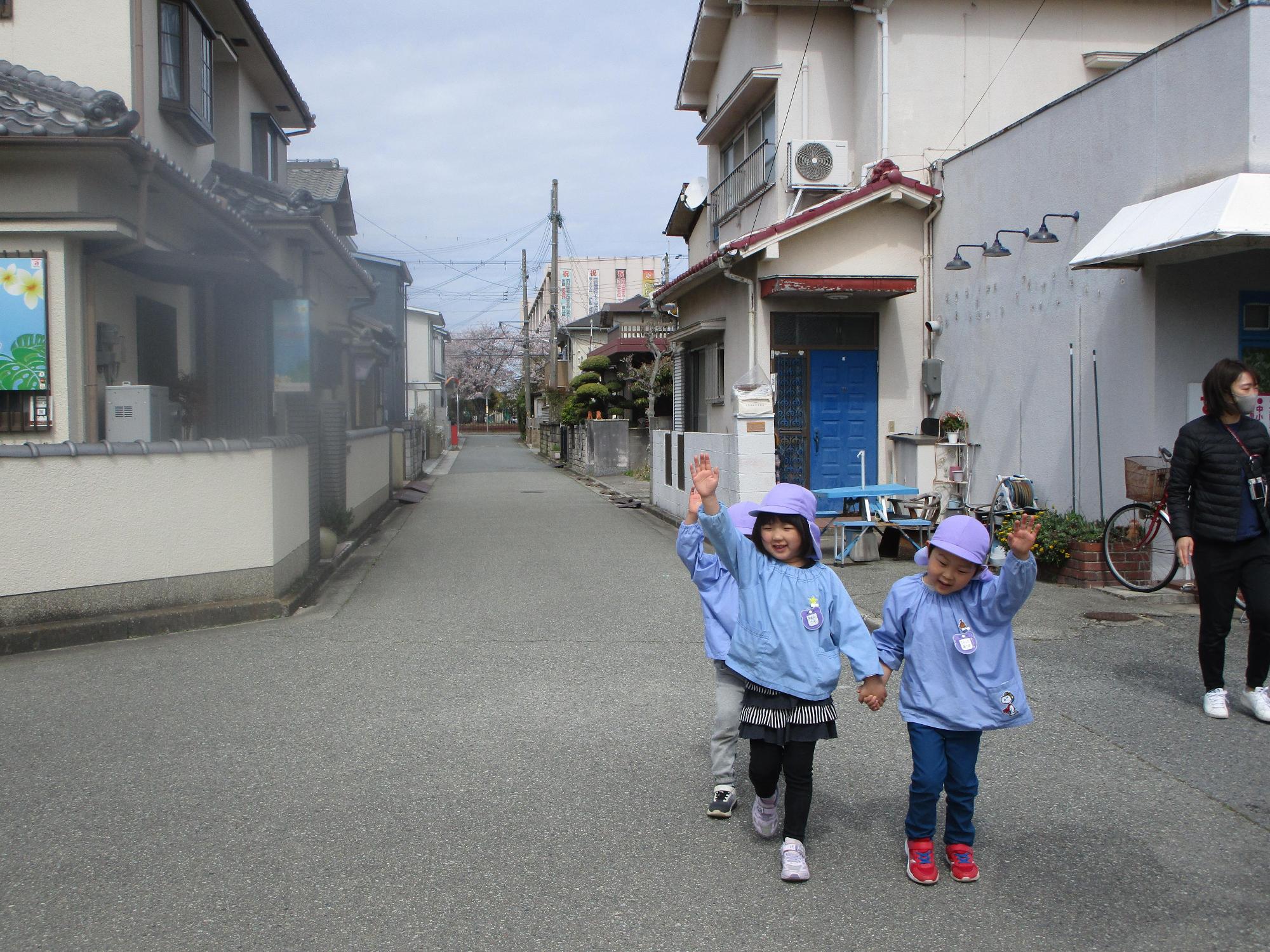 保育園児たちが左右を確認しながら手を挙げて道路を渡ろうとしている写真